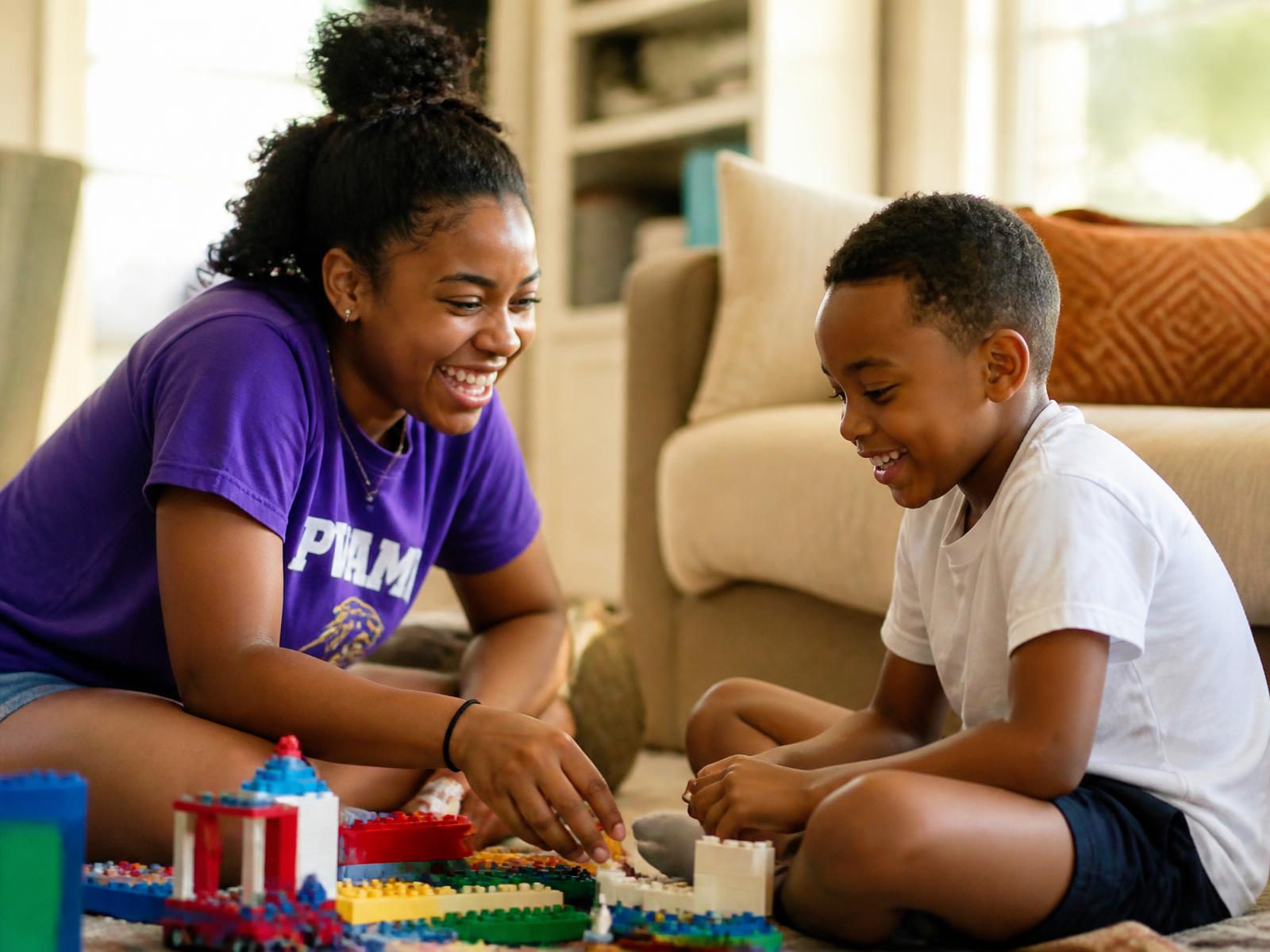 College athlete caregiver laughing with a child while building LEGO